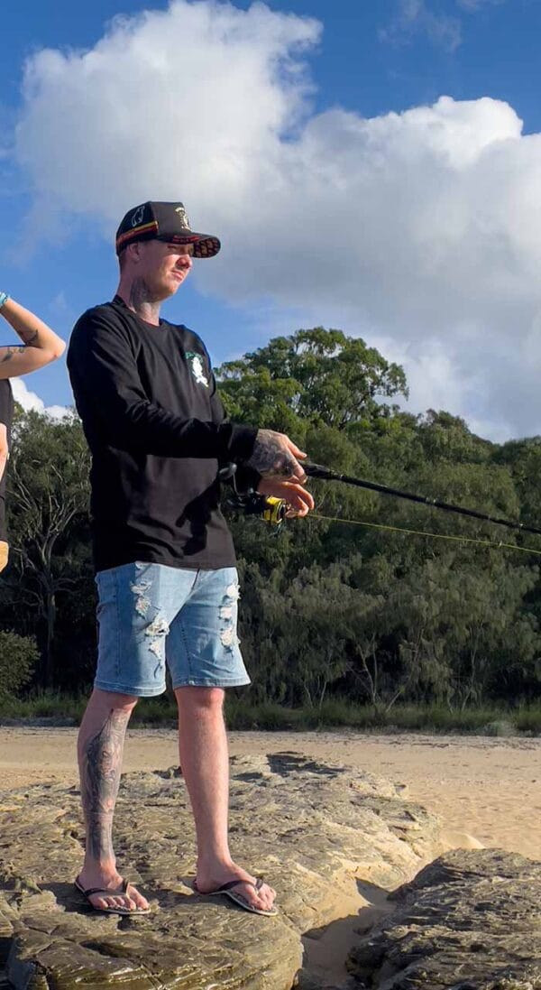 Front view of male wearing Catch Crew N' Co long sleeve t-shirt while fishing at the beach