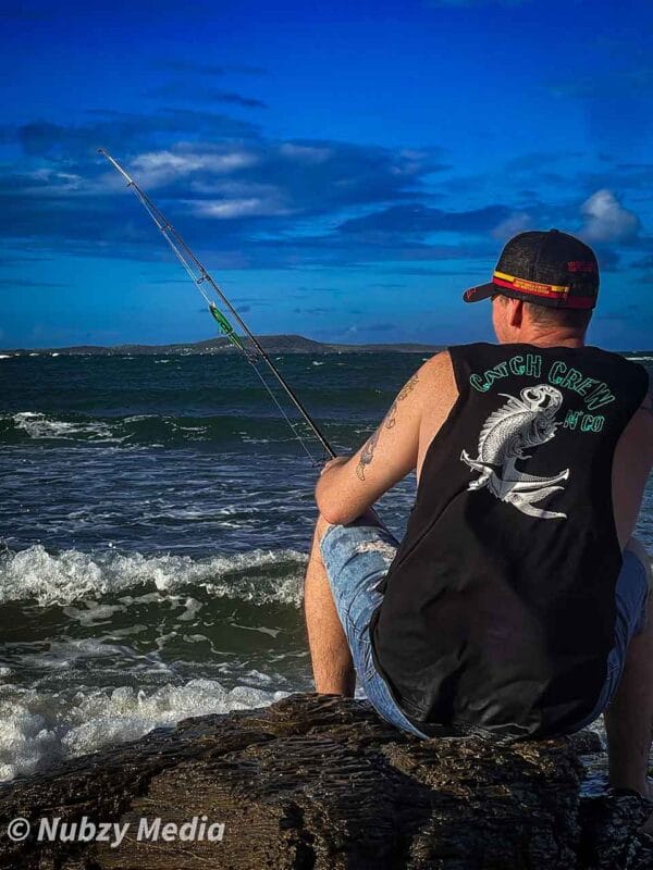 Rear view of male wearing Catch Crew N' Co singlet while fishing at the beach